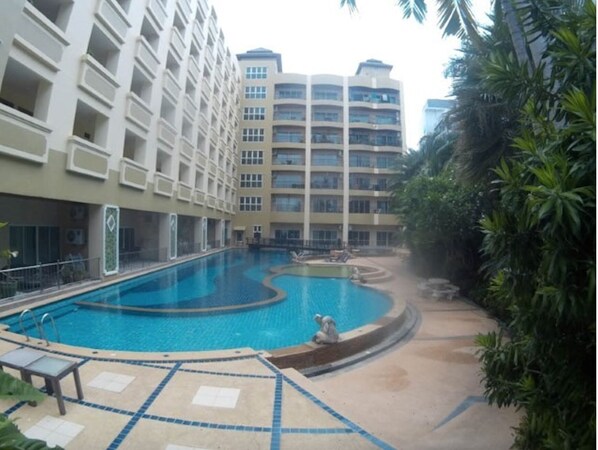 Relax by the pool surrounded by lush greenery and palm trees, with lounge chairs and a statue nearby.