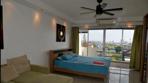 Quarto de hotel com cama, sofá, ventoinha no teto e uma grande janela com vista para a cidade.
