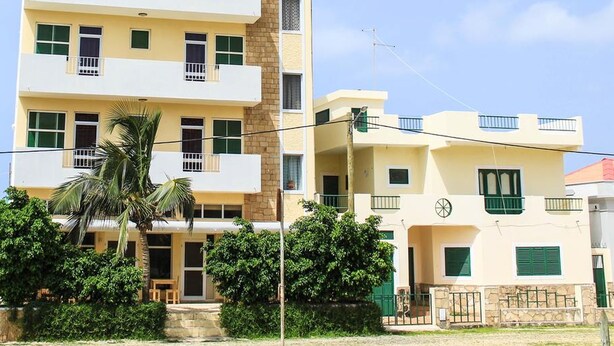 Un edificio residencial de varios pisos con balcones, una palmera y cielo despejado.