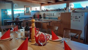 Une cuisine chaleureuse avec des poutres en bois, une table à manger dressée pour deux personnes, avec des serviettes rouges, des verres à vin et une théière rouge.