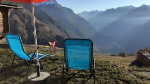 Deux chaises bleues et un parasol rouge sur une colline herbeuse, avec une vue sur la montagne.