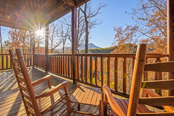 Una terraza de madera con sillas, con vistas a un paisaje montañoso con follaje otoñal.