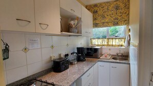 Een kleine keuken met witte kastjes, een gasfornuis, een koffiezetapparaat en een spoelbak.