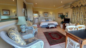 Een hotelkamer met een bed, twee witte rieten stoelen, een tafeltje, een televisie en een eethoek.