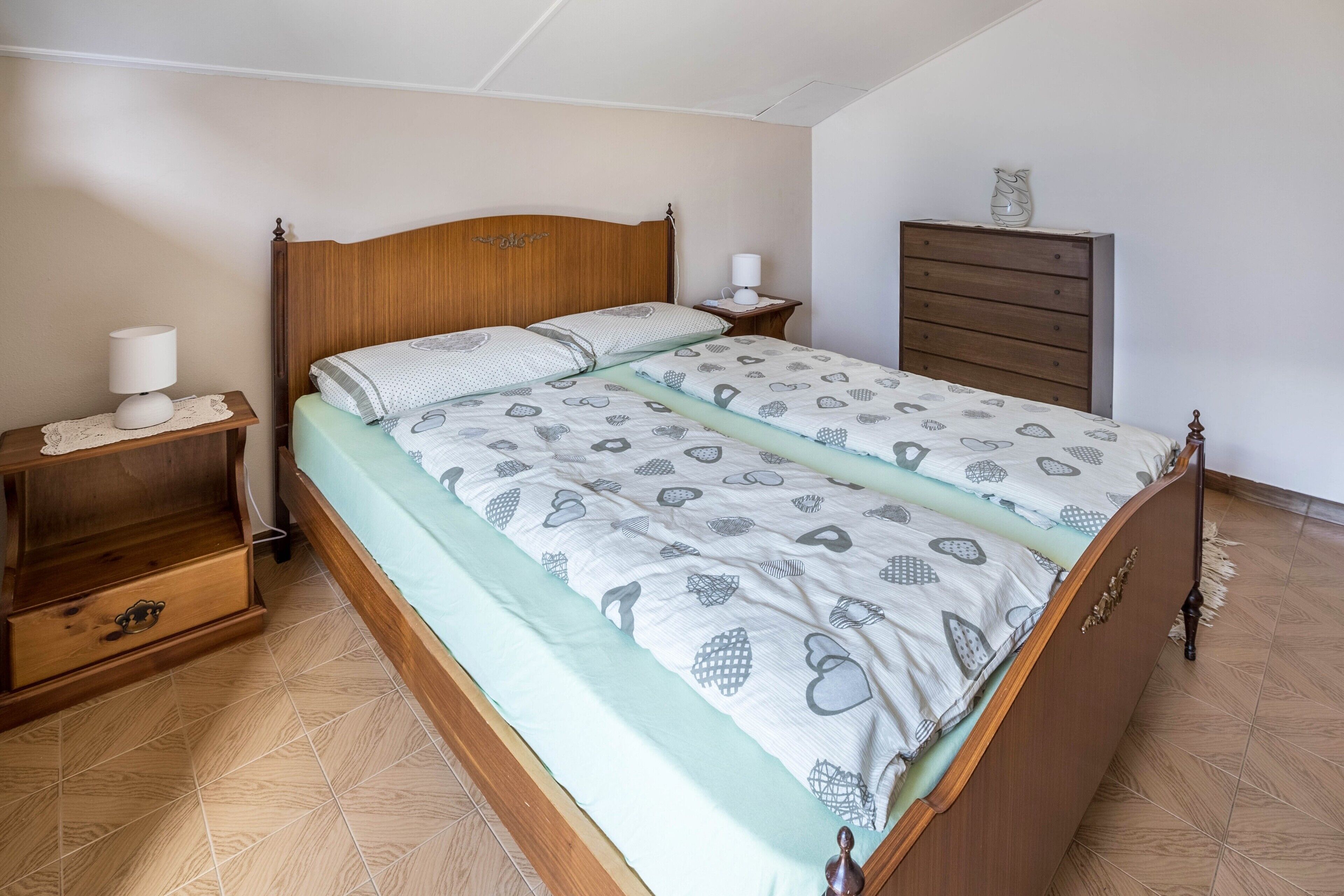 Une chambre à coucher avec un lit en bois, une table de chevet avec une lampe, une commode et une étagère fixée au mur.