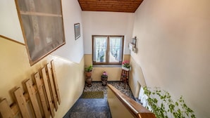 A narrow hallway with a wooden ceiling, a window with curtains, a wooden bench, and potted plants.