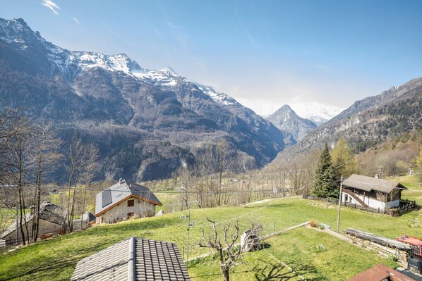 Eine Berglandschaft mit einem Haus mit geneigtem Dach, einem kleinen Gebäude mit Balkon und einem eingezäunten Bereich.