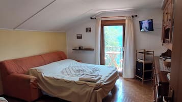 A bedroom with a bed, a chair, a TV, a shelf, and a balcony door.