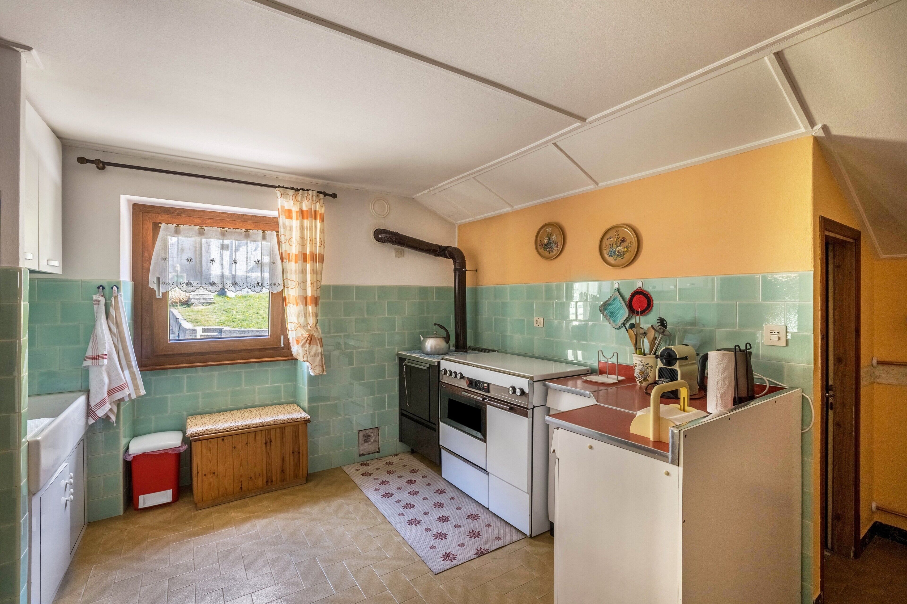 Una cocina con ventana, radiador, lavabo y estufa.