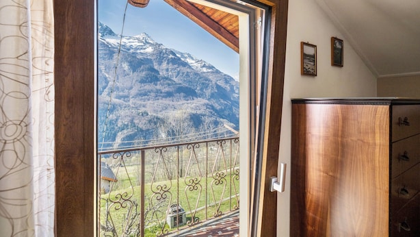 A room with a wooden door, a view of a mountain landscape through a window, and a wooden cabinet.