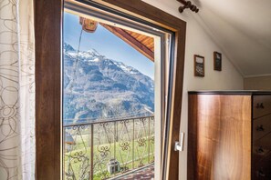Ein Zimmer mit Holztür, Blick auf eine Berglandschaft durch ein Fenster und einem Holzkasten.
