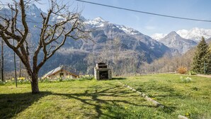 A mountainous landscape with a stone fireplace, a tree, and a building in the foreground.