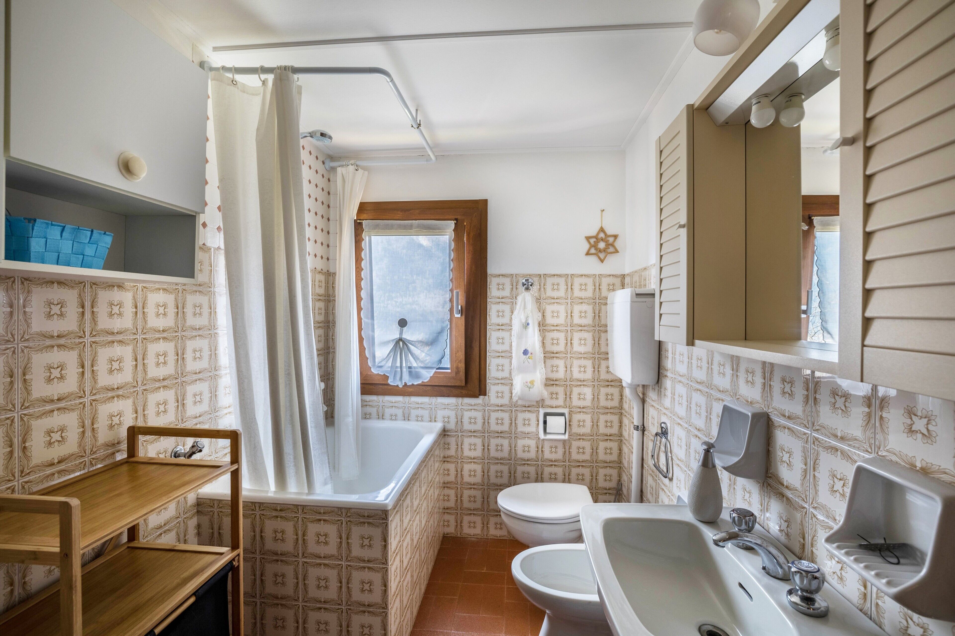 Une salle de bain équipée d’une baignoire, de toilettes, d’un lavabo et d’une fenêtre avec un rideau.