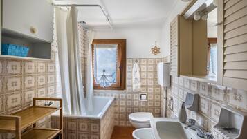 Une salle de bain équipée d’une baignoire, de toilettes, d’un lavabo et d’une fenêtre avec un rideau.