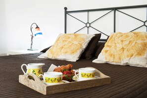 A neatly made bed with a tray of breakfast items, including croissants and strawberries, and two cups with a yellow pattern. - Room-rome Center Room Classic Suite (Rome)