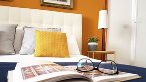 Un lit bien fait, recouvert d’une couverture bleue, avec un oreiller jaune et un livre posé dessus, accompagné d’une paire de lunettes.