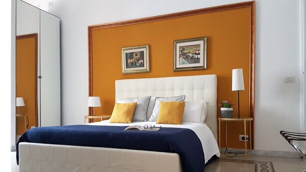 Une chambre d’hôtel avec un grand lit, deux tables de chevet avec des lampes, un miroir et deux tableaux encadrés au mur.