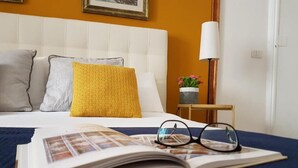 Un lit bien fait, recouvert d’une couverture bleue, avec un livre et des lunettes posés dessus.
