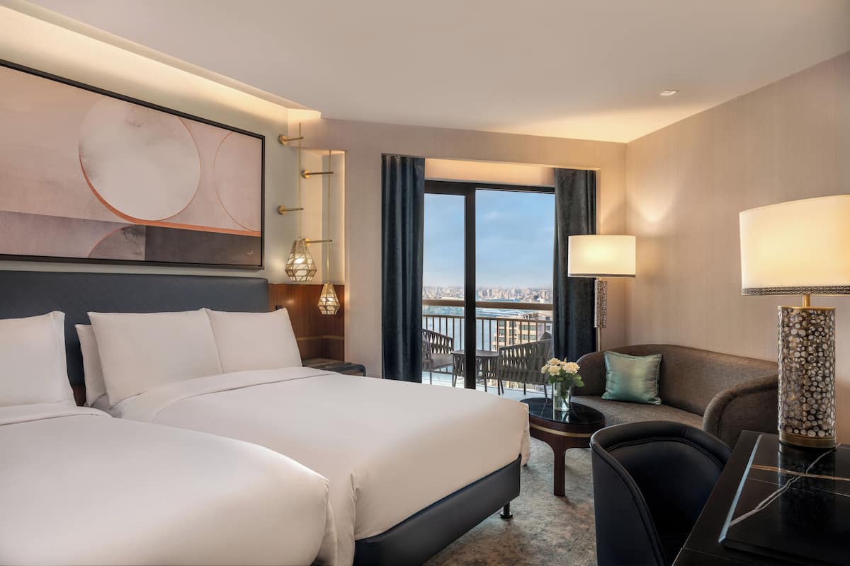 Una habitación de hotel con una cama grande, un sofá, un escritorio con lámpara y vistas a la ciudad desde la ventana.