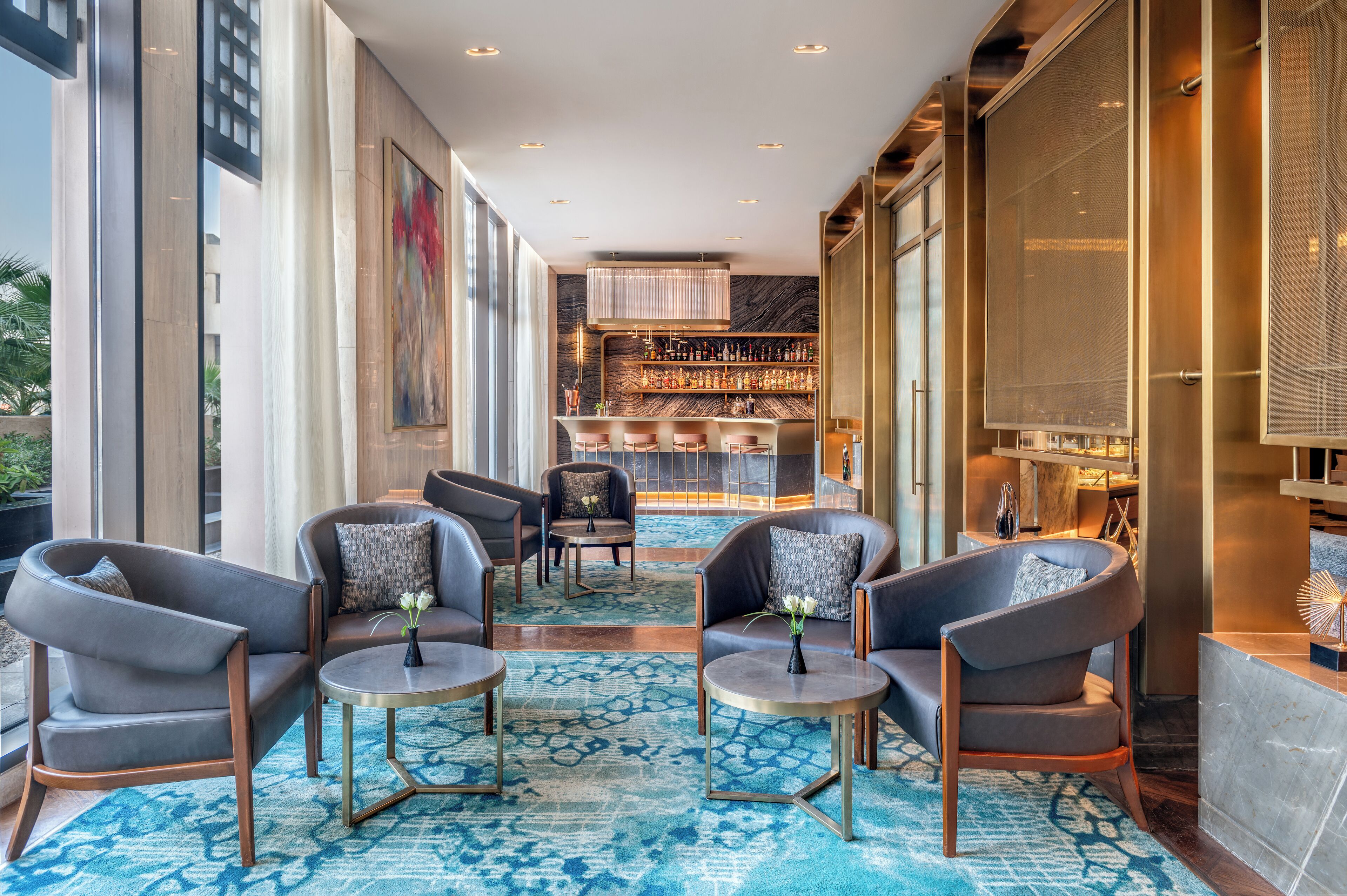 A modern lounge area with leather sofas and armchairs, a bar with shelves of bottles, and a large window providing natural light.