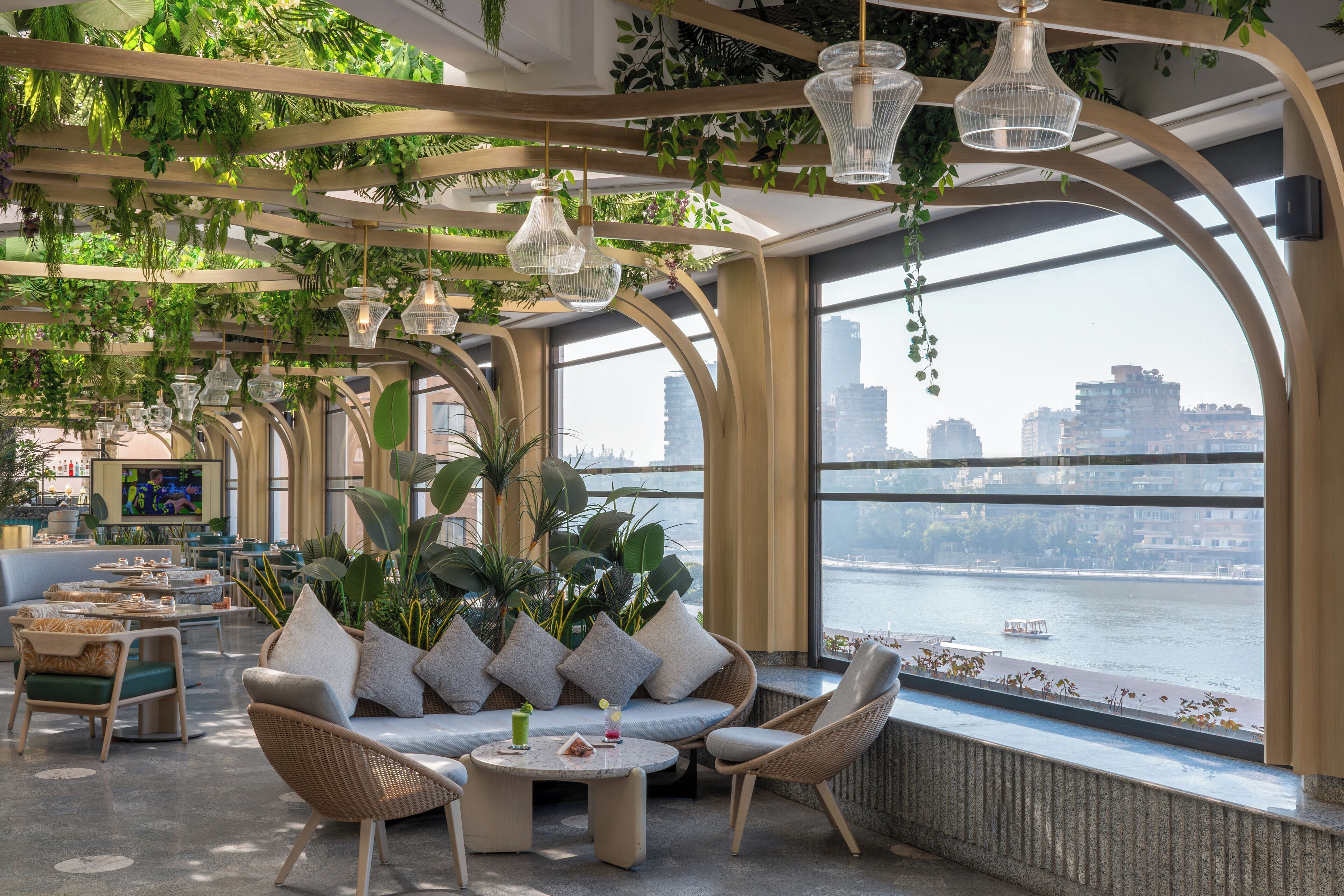 A modern lounge area with seating, a view of a river, and hanging plants.