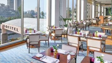A modern restaurant with tables set for dining, large windows offering a city view, and a sign reading 'SOFITEL'.