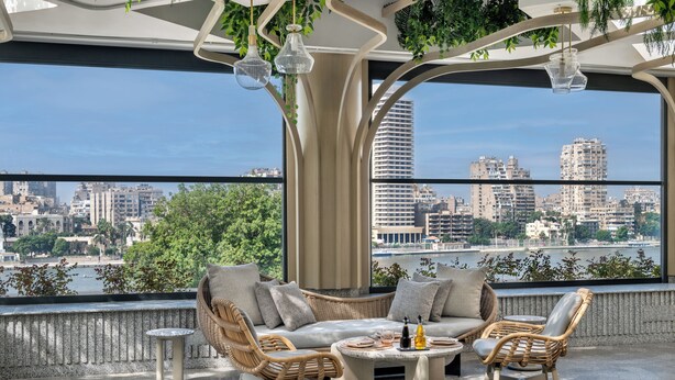 A modern lounge with wicker furniture, a round table, and a view of a cityscape and river.