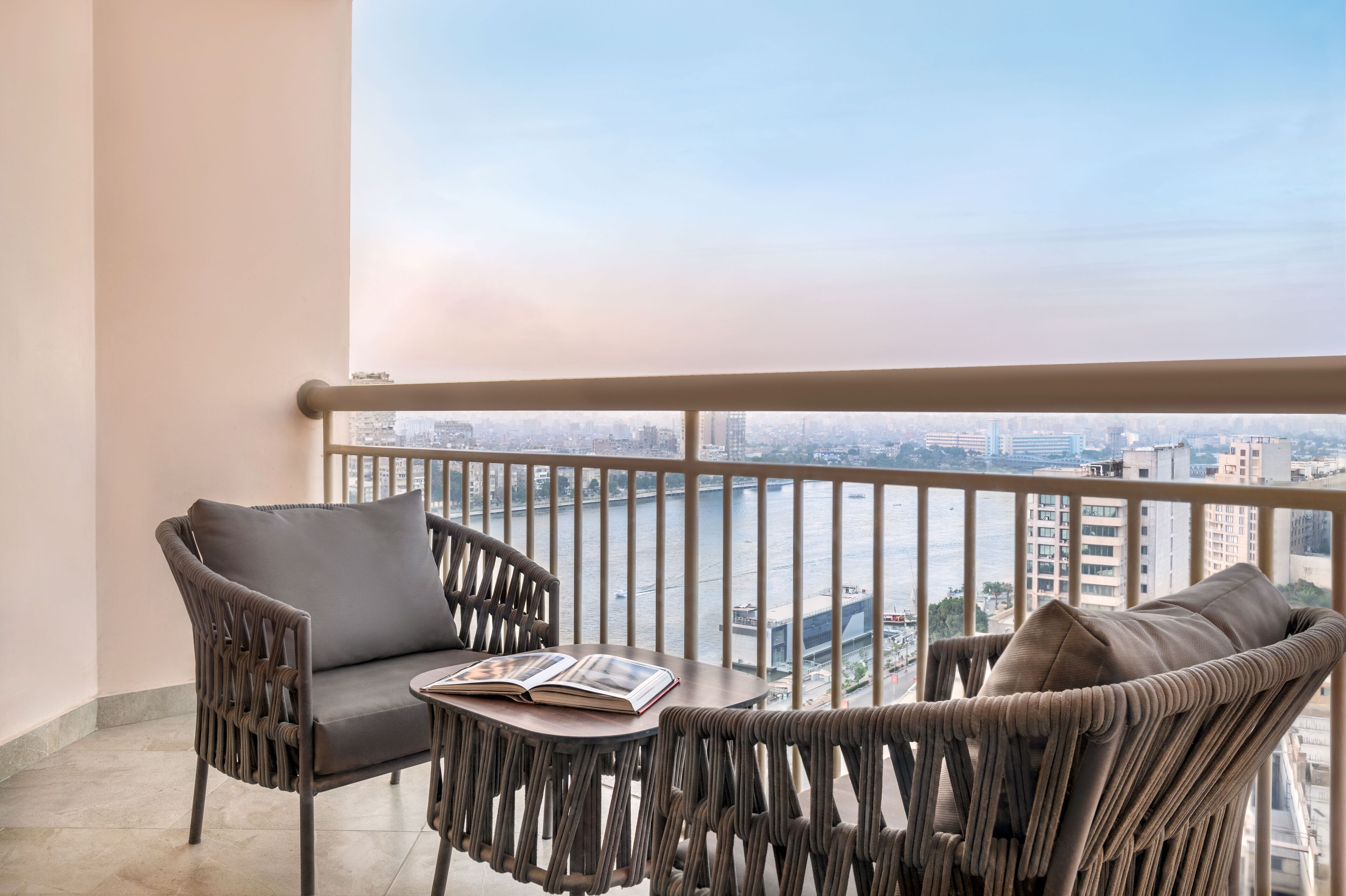 A balcony with a view of a cityscape and a table with two chairs and an open book.