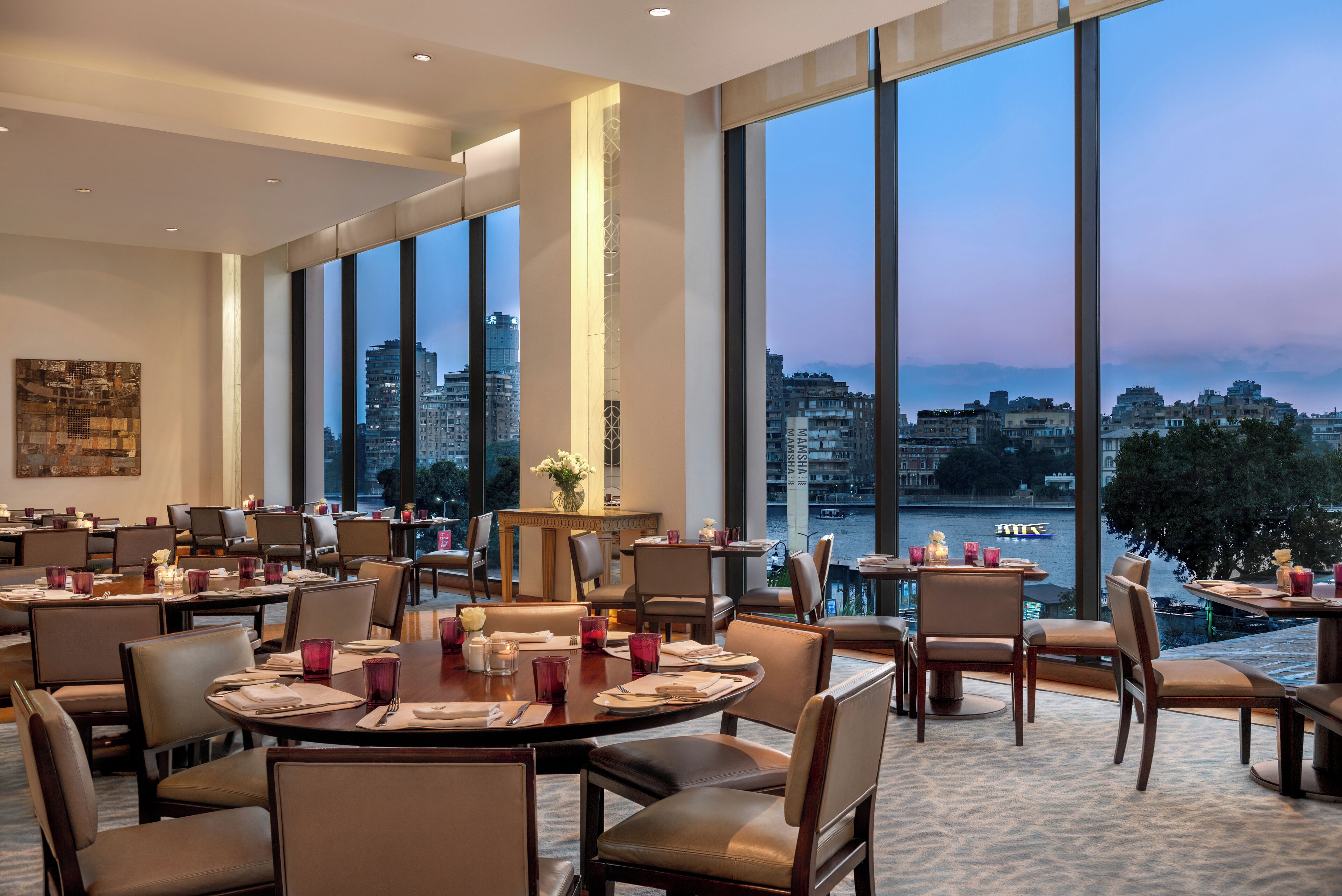 A restaurant with large windows offering a city view, multiple dining tables, and chairs.