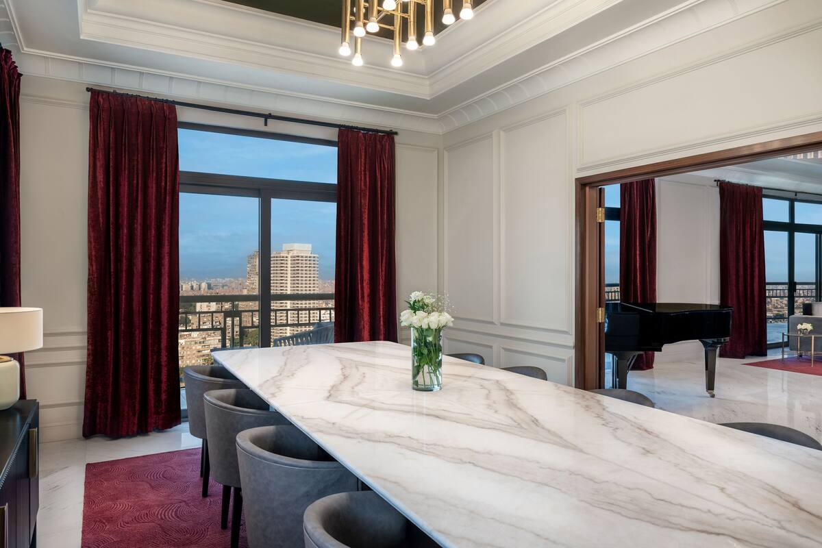 Un comedor amplio con una mesa de mármol, cortinas rojas y vistas a la ciudad.
