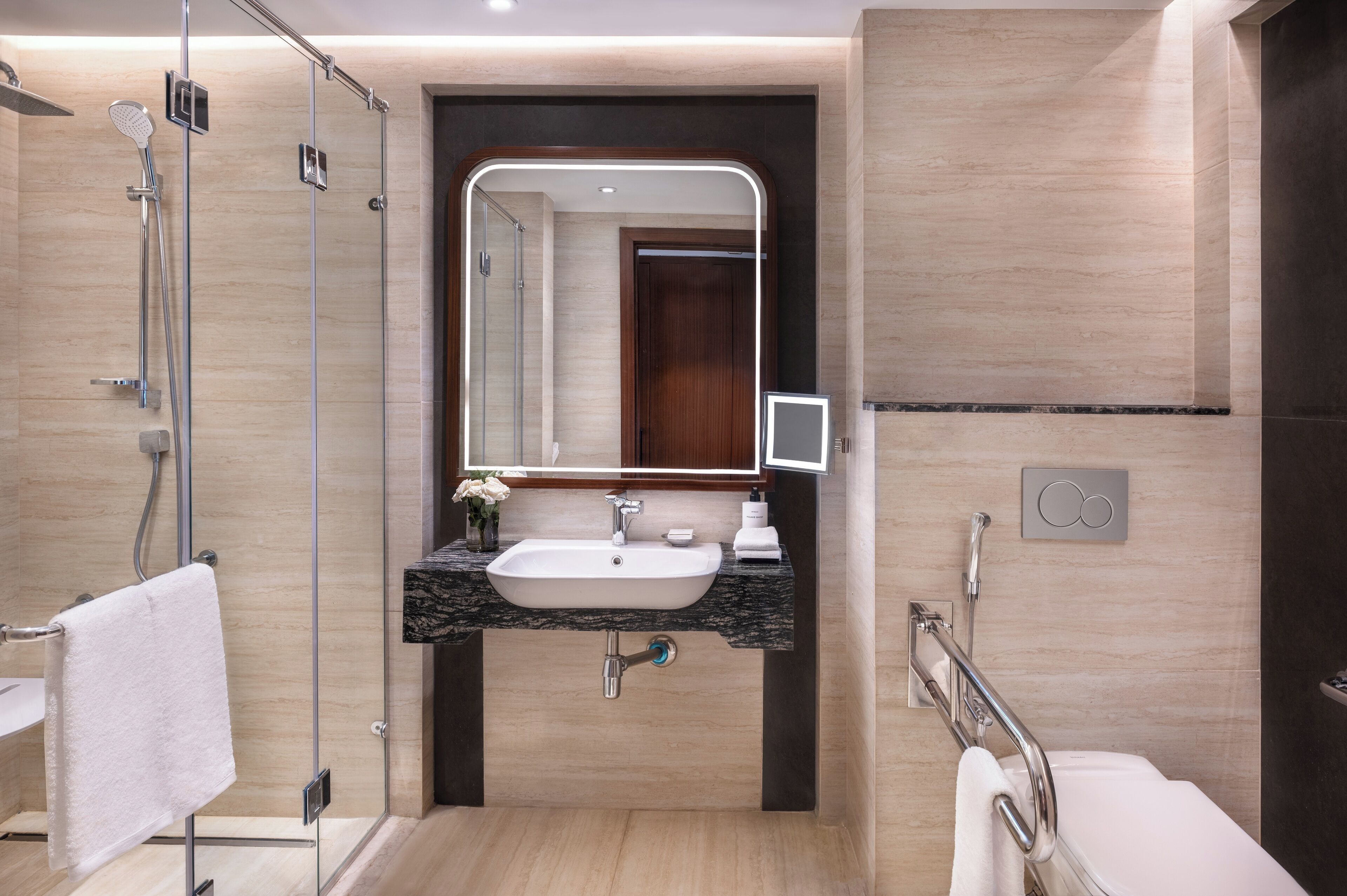 A modern bathroom with a glass shower enclosure, a sink with a marble countertop, and a large mirror.