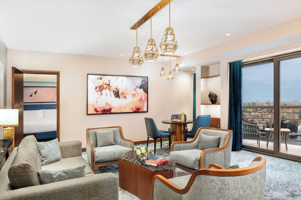 Una habitación de hotel con un ventanal grande, un televisor de pantalla plana, una mesita de centro y un área de descanso con sillones.