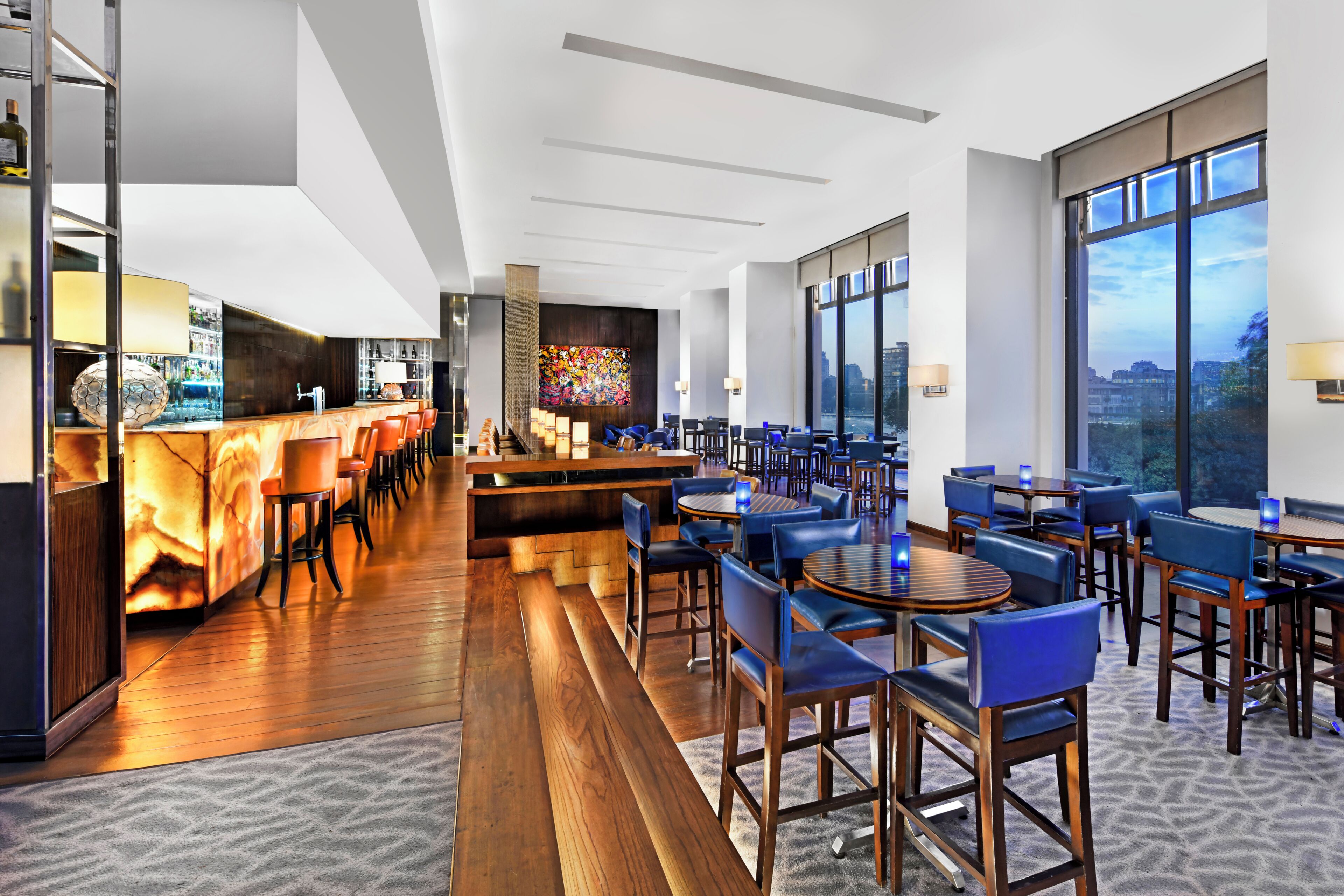 Un moderno vestíbulo de hotel con una zona de bar, arreglos de asientos y grandes ventanales con vistas a la ciudad.