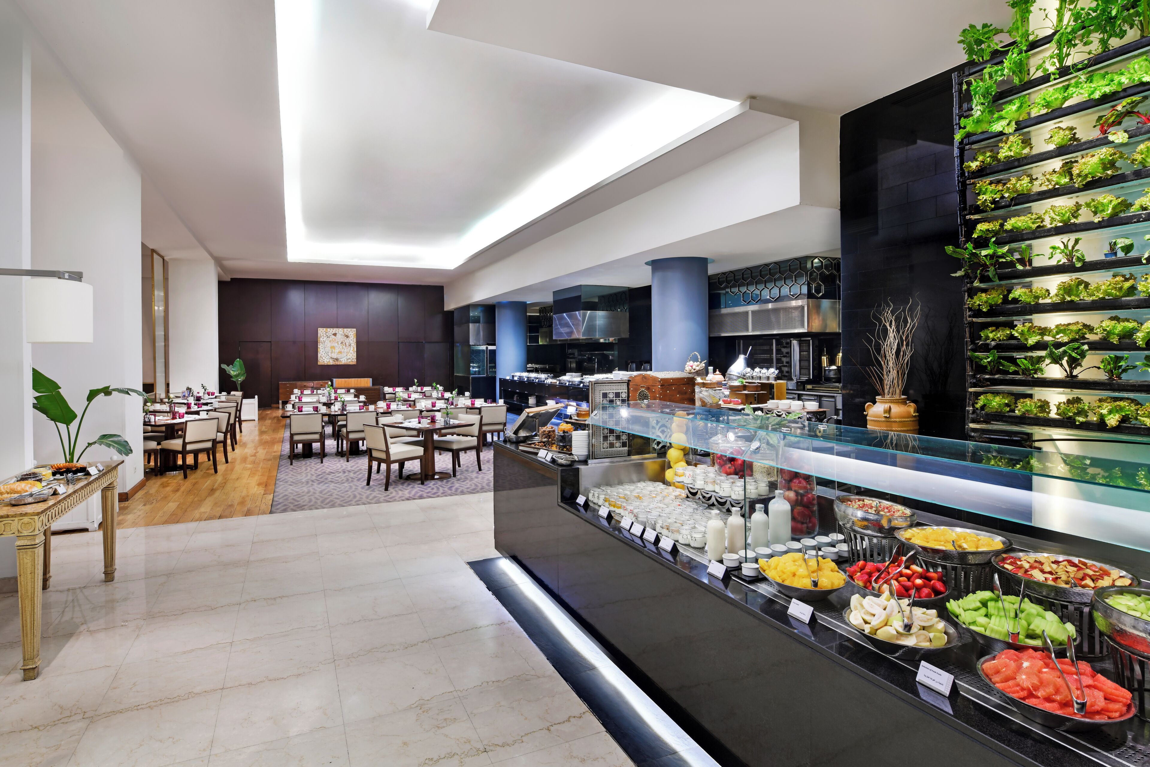 Un comedor moderno de hotel con bufé, mesas dispuestas y una exhibición de jardín vertical.