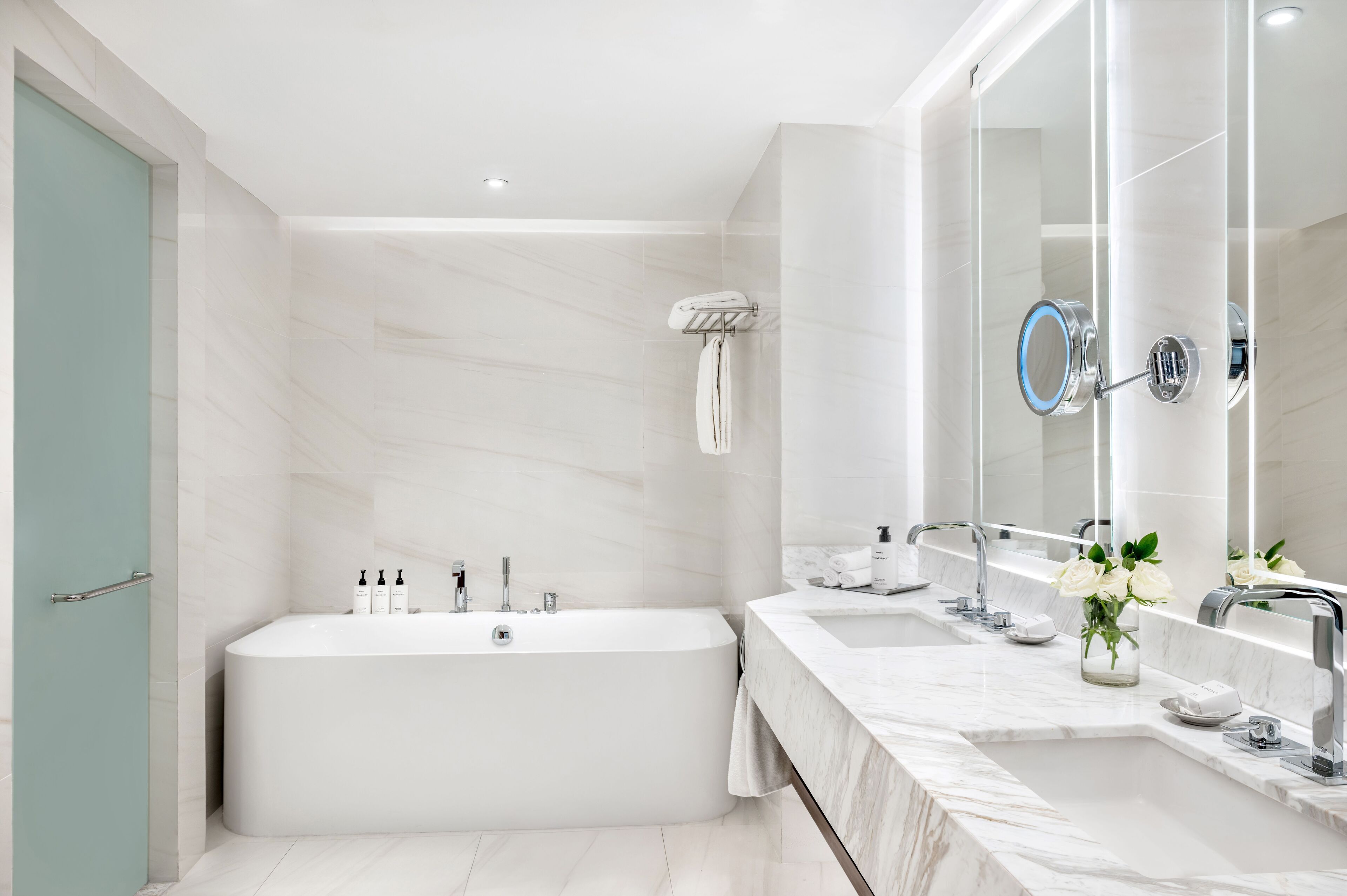 A modern bathroom with a large bathtub, two sinks, a vanity mirror, and a towel rack.