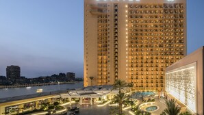 A high-rise hotel with multiple balconies, a swimming pool, and a well-lit facade.