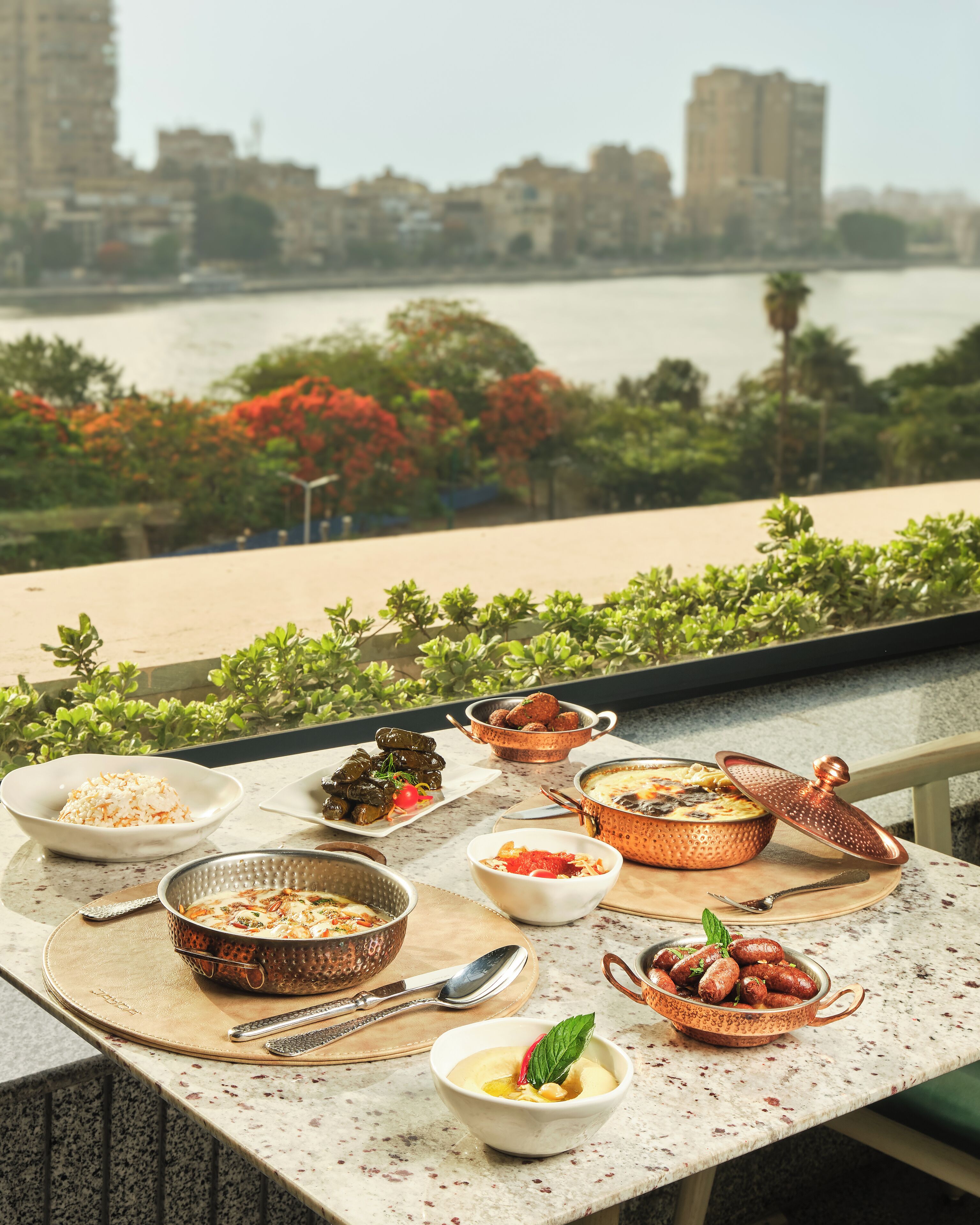 A dining table with various dishes and a view of a river and cityscape.