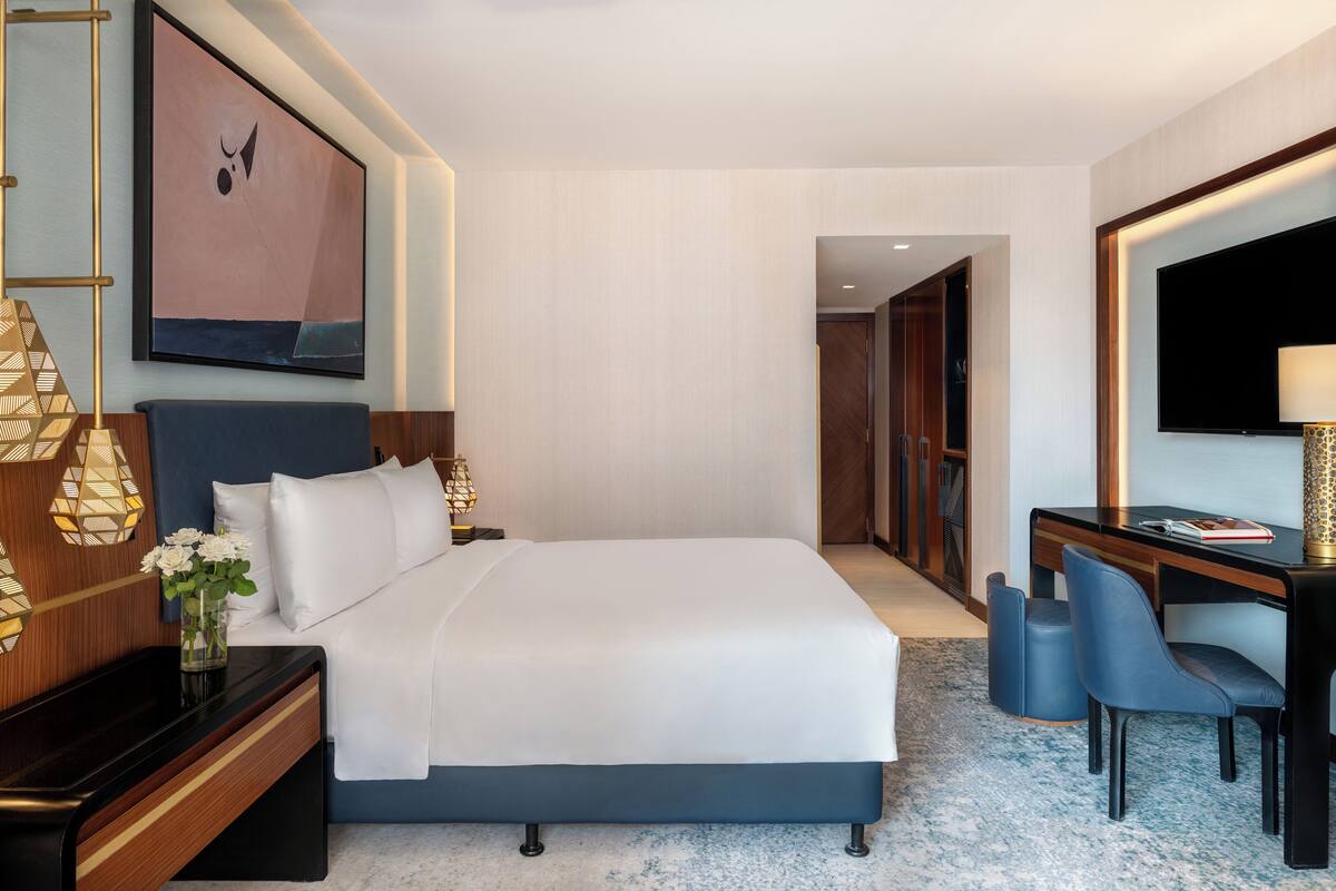 Una habitación de hotel moderna con una cama grande, un escritorio con silla, un televisor y un elemento decorativo en la pared.
