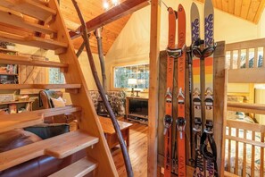 Una escalera de madera que conduce a un entrepiso con un soporte para esquíes, muebles de madera y una pared de piedra.