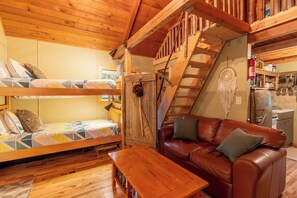 Interno accogliente di una baita con un letto a castello, un divano in pelle, un tavolino in legno e una scala.