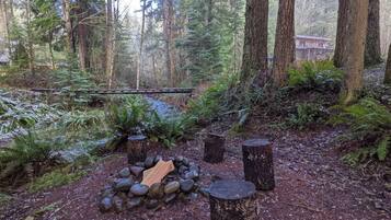 Zona boscosa con un hogar para fogatas rodeado de rocas y tocones.