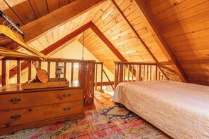 Una camera da letto mansardata con travi in legno, un letto, una cassettiera e una finestra.