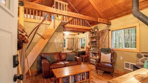 A cozy cabin interior with a wooden staircase, leather furniture, and a bookshelf. - Storybook Cabin on Sahara Creek - 8mi to MRNP! (Ashford)