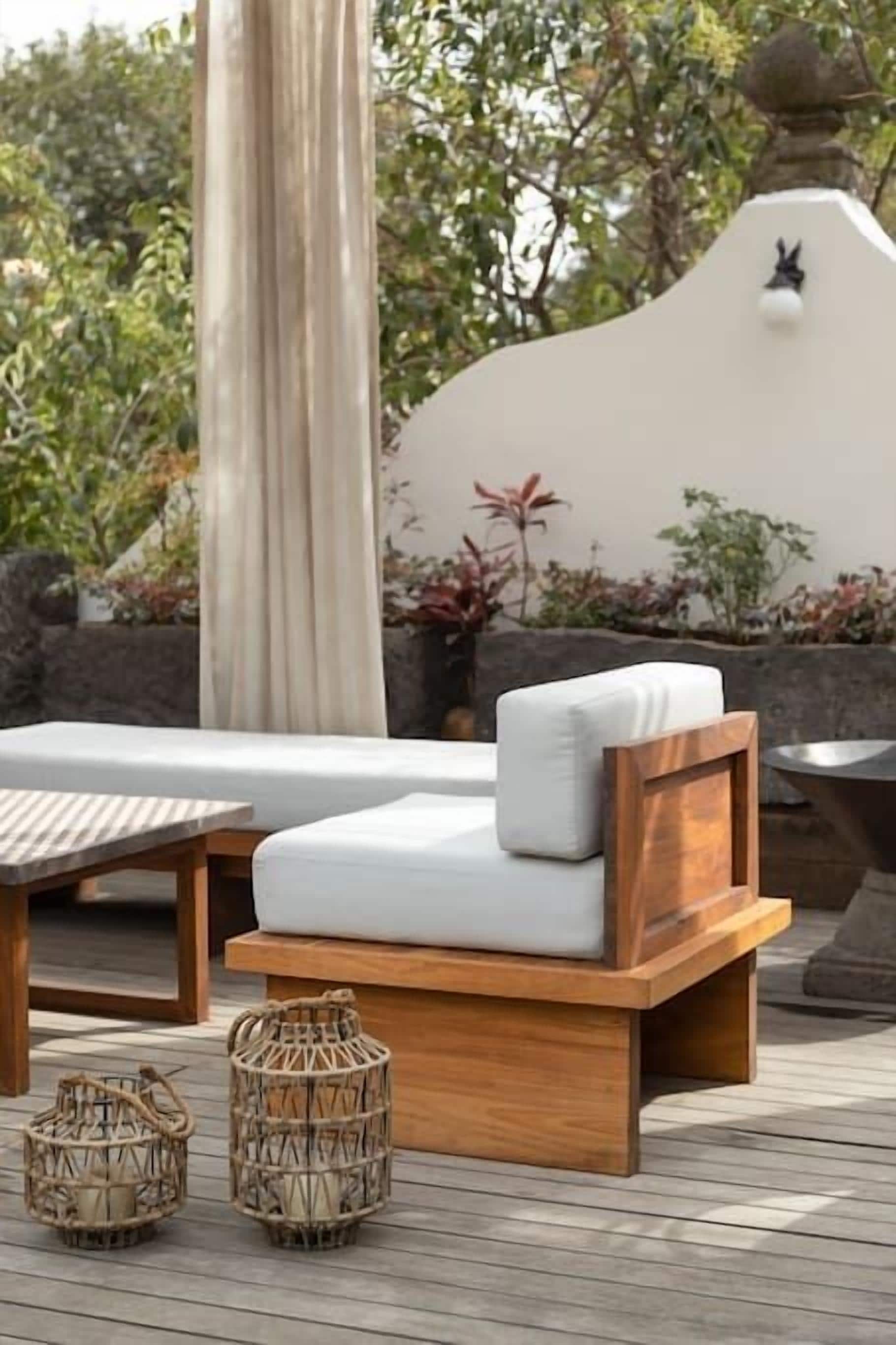 A wooden deck with a white cushioned bench, wicker baskets, and a stone wall with a decorative element.