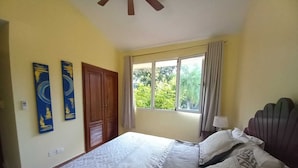 Una camera da letto con un letto, una finestra con tende, una ventola a soffitto e decorazioni alle pareti.