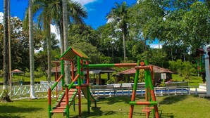 A playground with climbing structures and slides, surrounded by palm trees and a white fence. - Room-room With 1 Double bed and 2 Single (Pereira)
