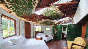 A cabin with two beds, wooden floors, a green chair, and a hanging plant. - Room-tree House Finca La Floresta Verde (Pereira)