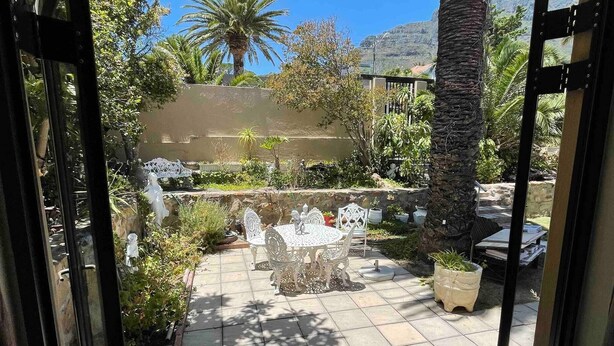 Een terras met een stenen tafel en stoelen, omgeven door potplanten en een palmboom.