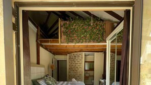 Een slaapkamer met een bed, een kleine badkamer en een balkon met planten.