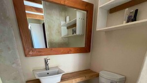 Een kleine badkamer met een houten wastafelmeubel, een witte wastafel, toilet en een spiegel boven het meubel.